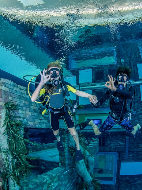 Scuba divers exploring underwater cityscape at Deep Dive Dubai.