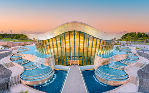Modern architecture of Deep Dive Dubai with cascading pools at sunset.