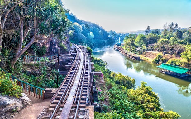 Railway track along the River Kwai in Erawan National Park, surrounded by lush greenery.
