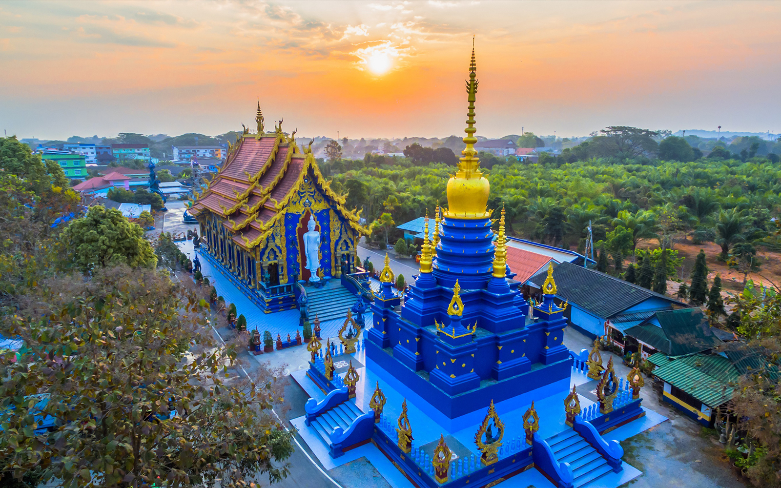 Blue Temple in Chiang Rai at sunset, featuring intricate gold details and surrounding greenery.