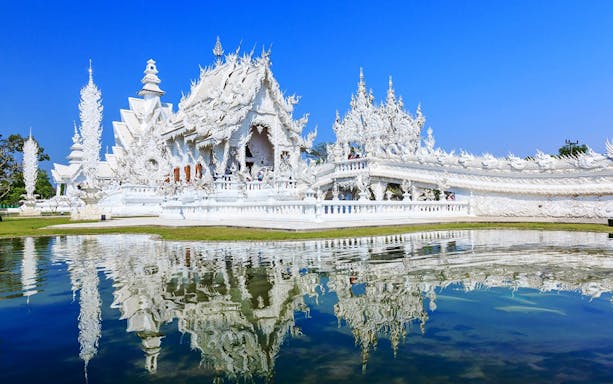 White Temple in Chiang Rai with intricate white architecture reflected in a pond.