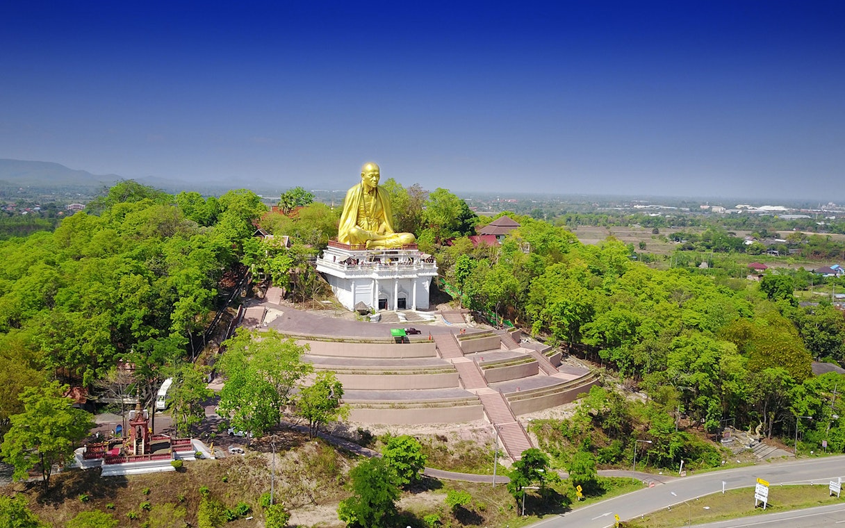 Golden Buddha statue at Doi Suthep surrounded by lush greenery, part of the Wat Pha Lat Sunrise Tour.