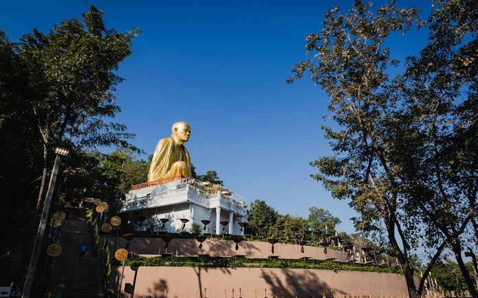 Golden Buddha statue at Wat Pha Lat, surrounded by trees, under a clear blue sky.
