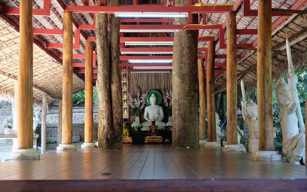 Buddha statue at Wat Pha Lat temple, surrounded by wooden pillars and sculptures, Chiang Mai.