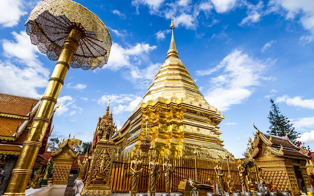 Golden stupa and ornate structures at Wat Phra That Doi Suthep, Chiang Mai, under a blue sky.