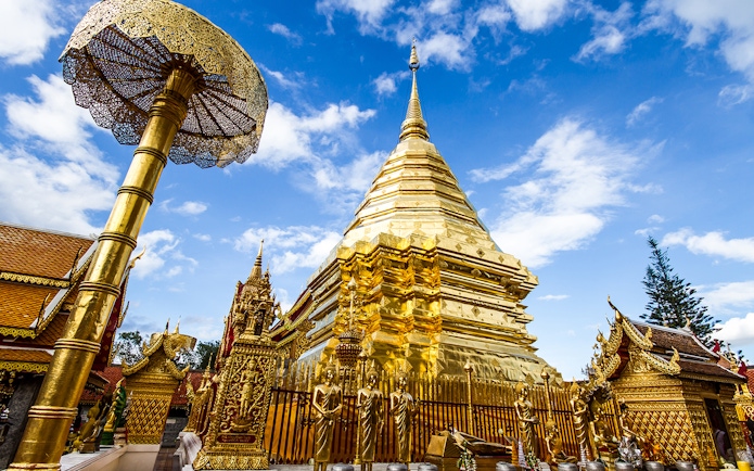 Golden stupa and ornate structures at Wat Phra That Doi Suthep, Chiang Mai, under a blue sky.