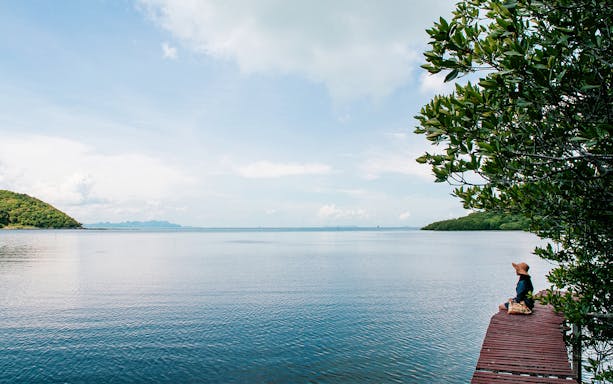 Person sitting on a wooden pier overlooking the sea on Koh Samui Island, Thailand.