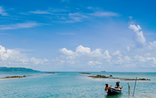 Boat anchored near rocky shore on Koh Samui Island under blue sky.