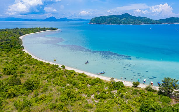 Koh Samui beach with boats and lush greenery, part of the island hopping tour.