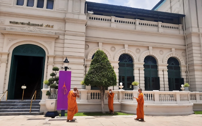 Monks in orange robes outside a building at the Grand Palace, Bangkok, during a walking tour.