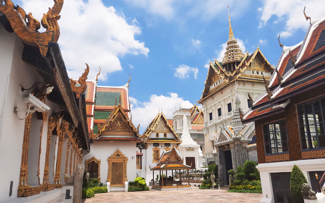 Grand Palace Bangkok courtyard with ornate temple roofs and spires under blue sky.
