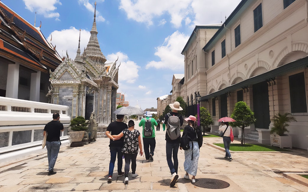 Visitors walking near ornate temple structures at Grand Palace, Bangkok.