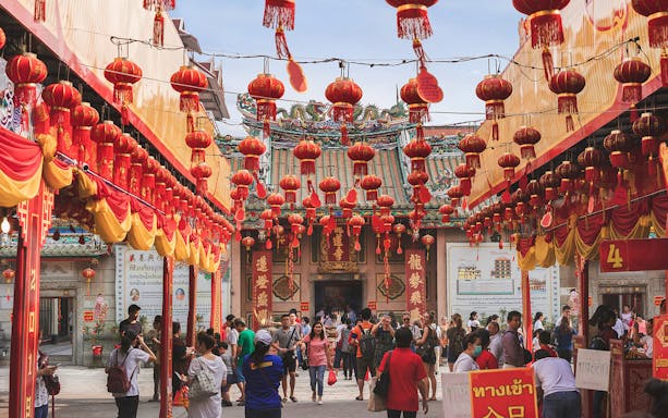 Crowd exploring Bangkok Chinatown with red lanterns and Chinese temple in background.