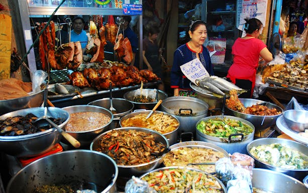 Street food stalls with various dishes in Bangkok's Chinatown market.