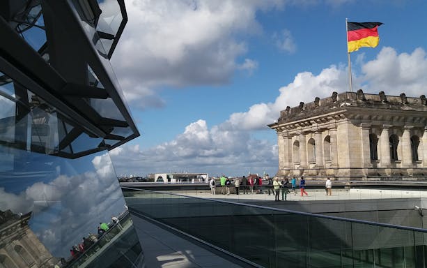 Reichstag building with German flag and tourists on the rooftop in Berlin.