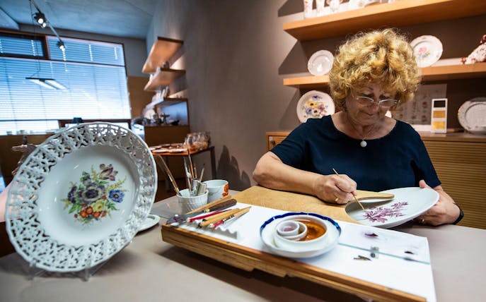 Artisan painting porcelain plate in Meissen workshop during Half-Day Tour from Dresden.