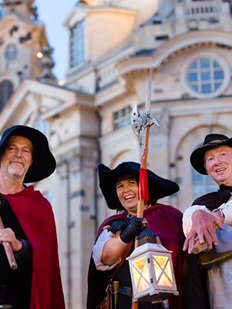 Night watchmen in traditional attire with lanterns in front of Dresden's Frauenkirche.