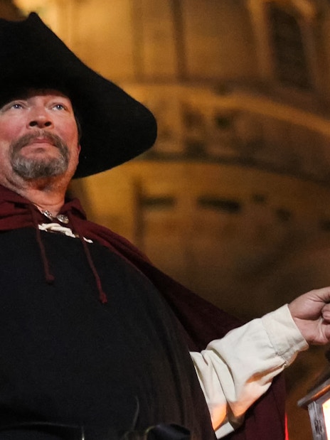 Night watchman holding lantern in front of Dresden landmark during guided tour.