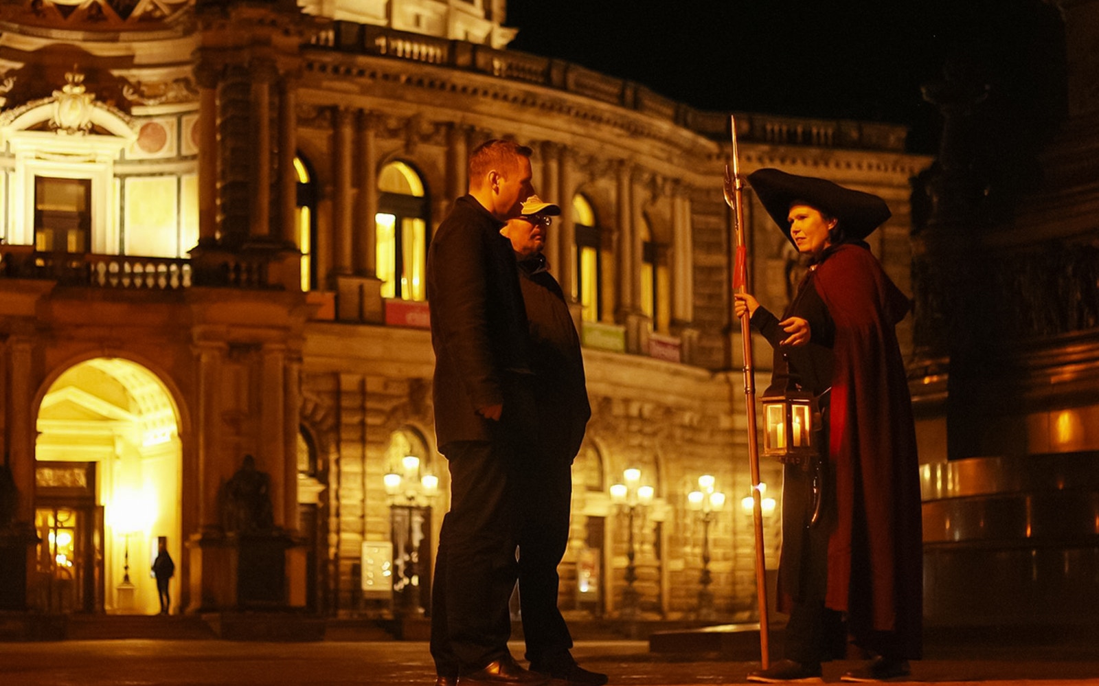 Night watchman guiding a tour in front of illuminated Dresden architecture.