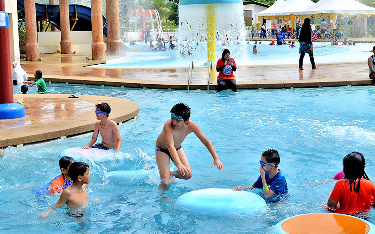 Children playing in the pool at Bayou Lagoon Water Park with slides and fountains in the background.