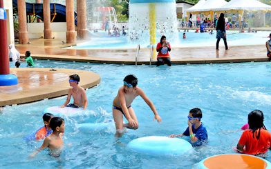 Children playing in the pool at Bayou Lagoon Water Park with slides and fountains in the background.