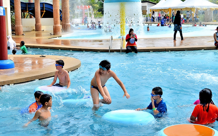 Children playing in the pool at Bayou Lagoon Water Park with slides and fountains in the background.