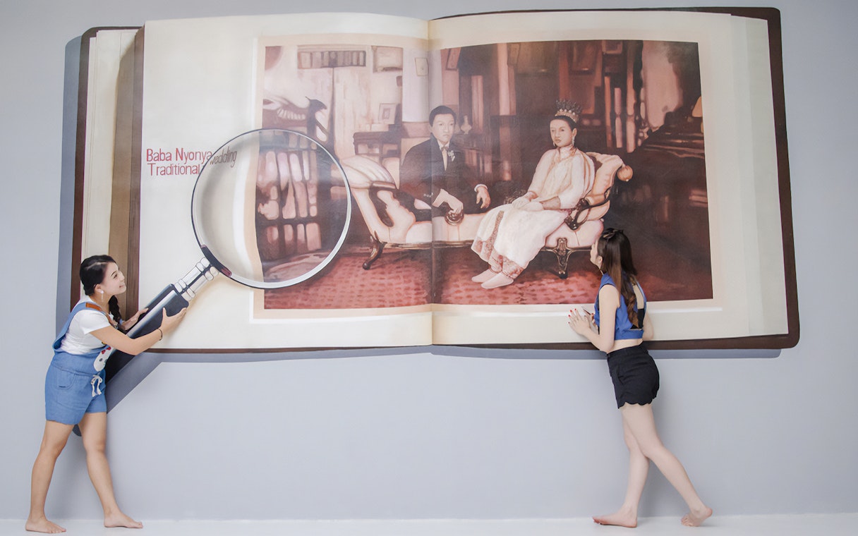 Visitors interact with a 3D art installation of a magnified book at Magic Art 3D Museum.