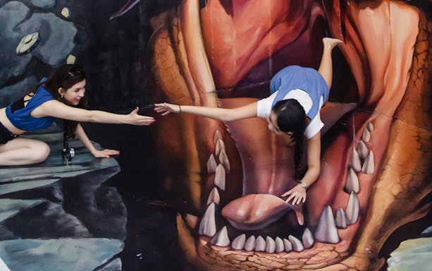 Visitors interacting with 3D art at Magic Art 3D Museum, creating an illusion of being inside a creature's mouth.