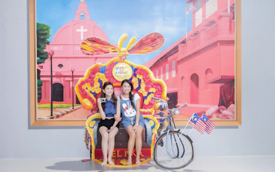Visitors posing with a colorful trishaw at Magic Art 3D Museum, featuring a mural of Christ Church Melaka.