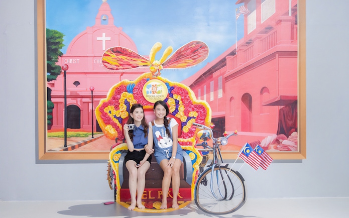Visitors posing with a colorful trishaw at Magic Art 3D Museum, featuring a mural of Christ Church Melaka.