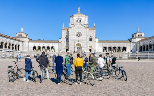 Group of cyclists in front of Milan's Monumental Cemetery during a bike tour.