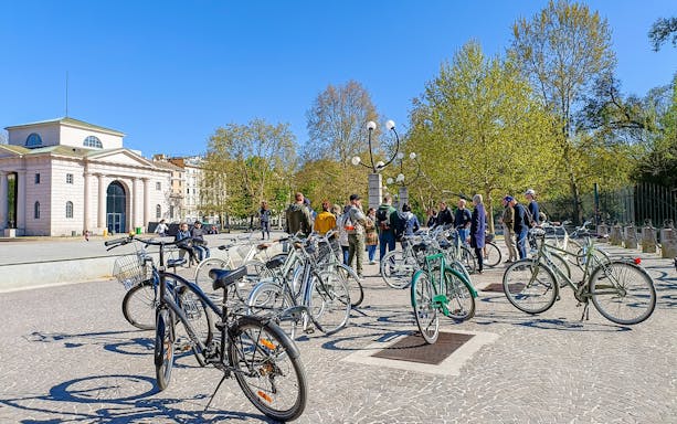 Bicycles parked near a group of people in a Milan square during a hidden treasures bike tour.