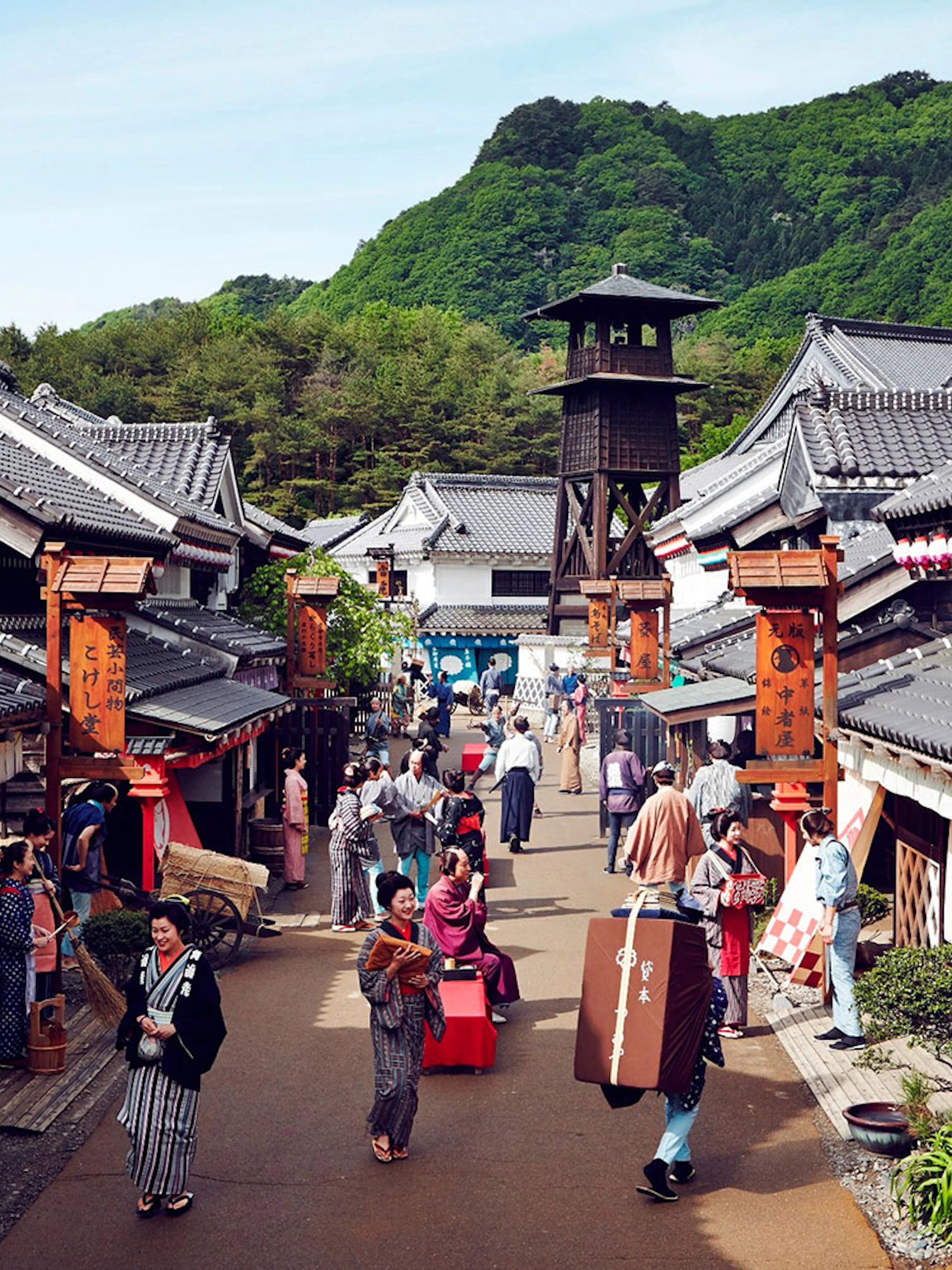 Visitors in traditional attire walking through Edo Wonderland, Japan, with historic buildings and a watchtower.