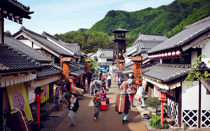 Visitors in traditional attire walking through Edo Wonderland, Japan, with historic buildings and a watchtower.