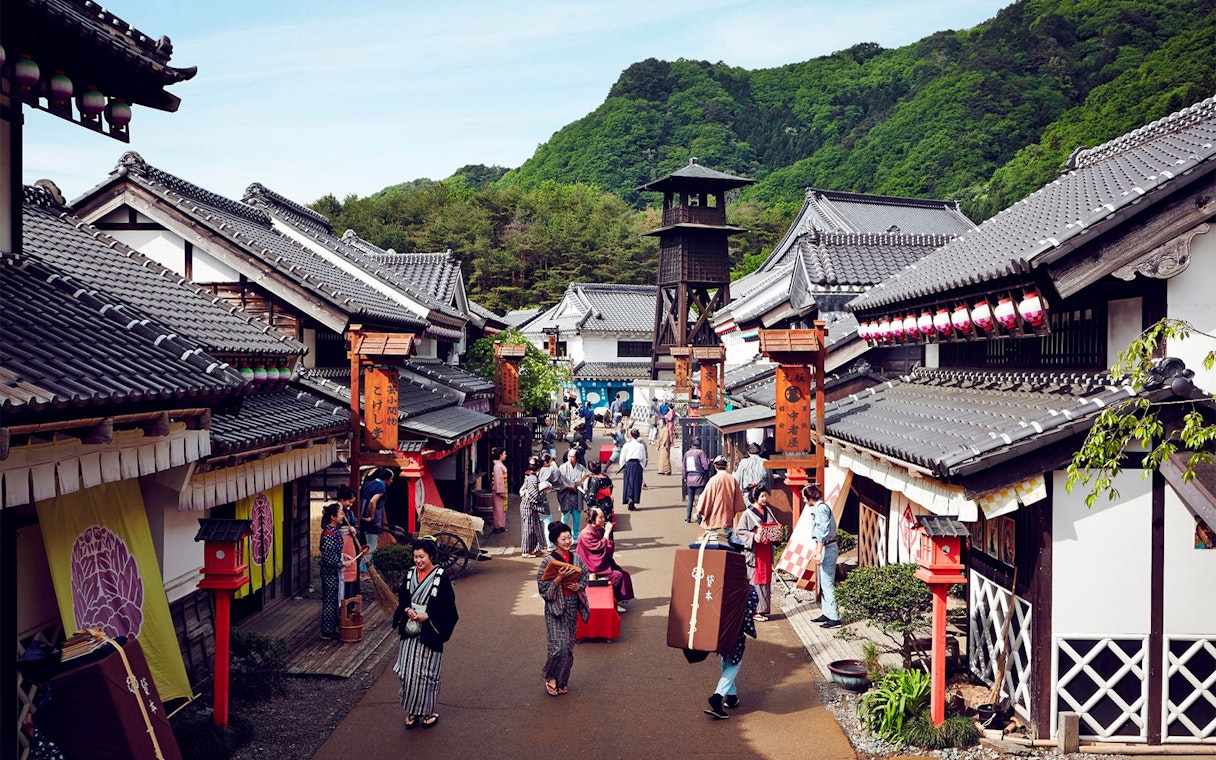 Visitors in traditional attire walking through Edo Wonderland, Japan, with historic buildings and a watchtower.