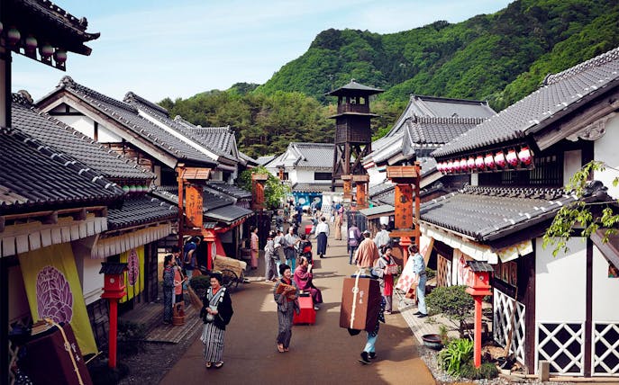 Visitors in traditional attire walking through Edo Wonderland, Japan, with historic buildings and a watchtower.