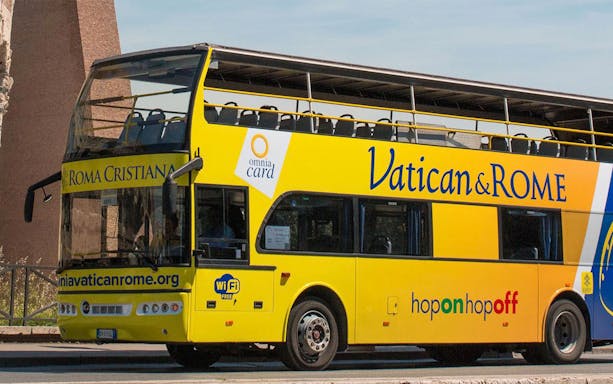 Vatican and Rome open-top tour bus parked near historical site.