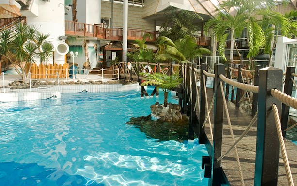 Indoor pool area with tropical plants and wooden bridge at Aquaboulevard, Paris.