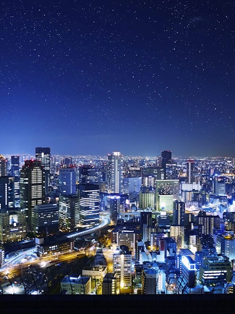 Night view of Osaka cityscape from Umeda Sky Building, illuminated buildings and starry sky.