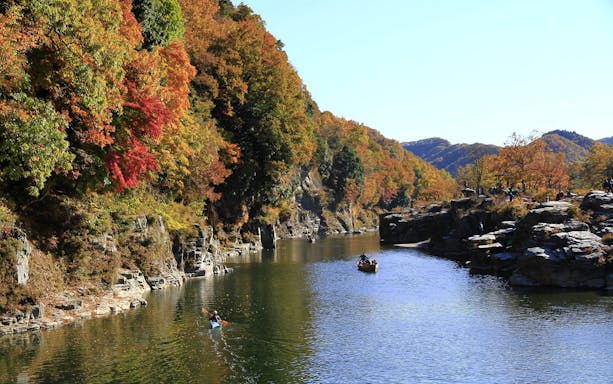 Kayakers on a river surrounded by autumn foliage in Chichibu, Japan.
