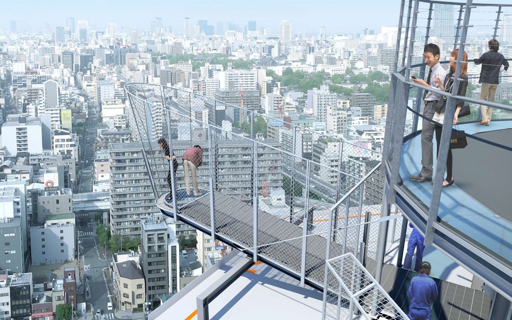 Visitors on Tsutenkaku Tower's observation deck overlooking Osaka cityscape.