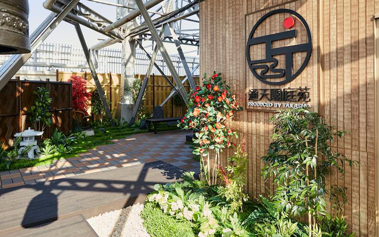 Tsutenkaku Tower garden area with plants and signage in Osaka, Japan.