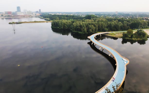 Curved pedestrian bridge over water in Almere, Netherlands, part of shuttle route to Floriade Expo 2022.