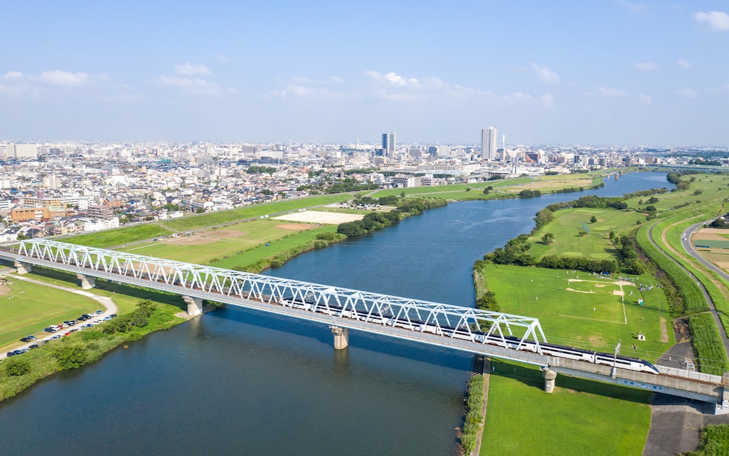Tokyo Skyliner crossing a bridge over a river with cityscape in the background.