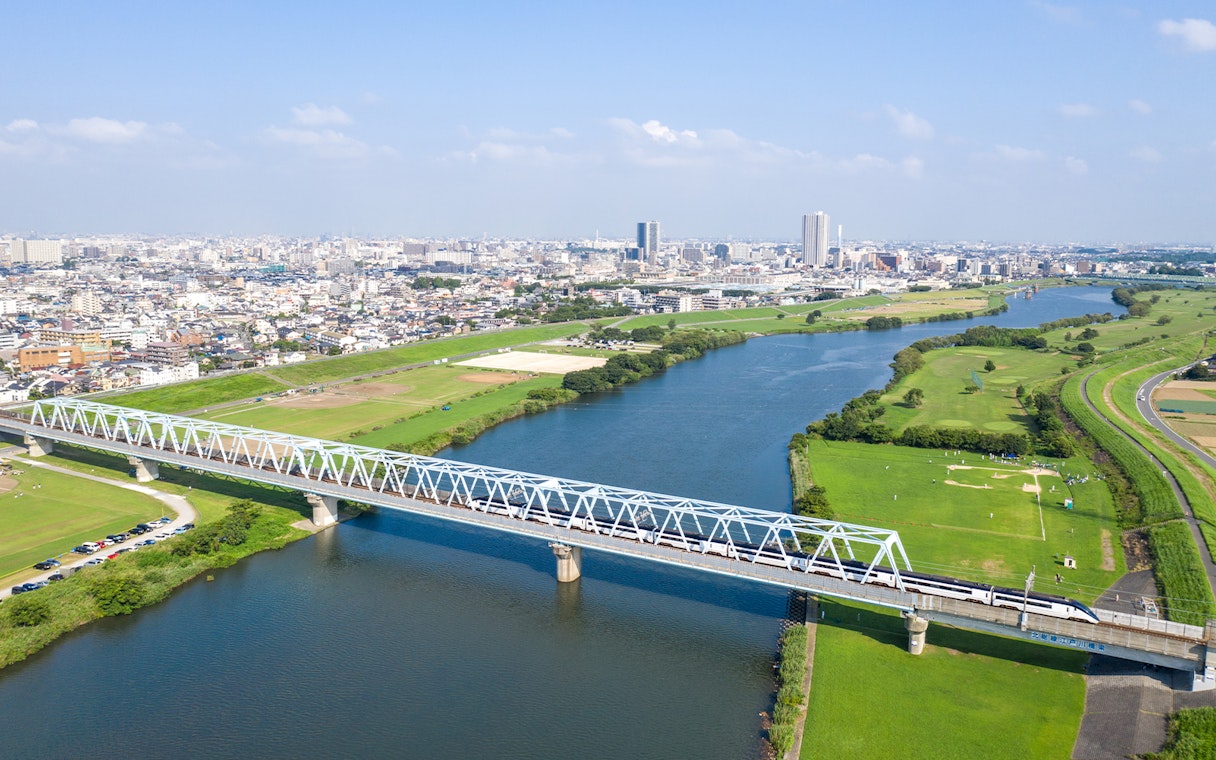 Tokyo Skyliner crossing a bridge over a river with cityscape in the background.