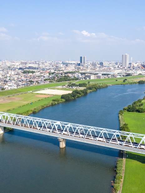 Tokyo Skyliner crossing a bridge over a river with cityscape in the background.