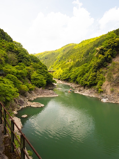 Sagano Romantic Train passing through lush green valley alongside a river in Kyoto, Japan.