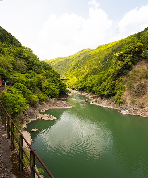 Sagano Romantic Train passing through lush green valley alongside a river in Kyoto, Japan.