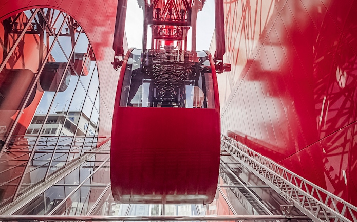 Red Ferris wheel cabin at HEP, viewed from below, with glass reflections.