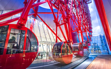Red gondolas of the HEP Ferris Wheel in a modern glass building.